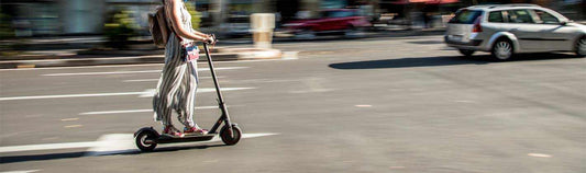 Woman riding electric scooter on city street with cars in background electric scooter review