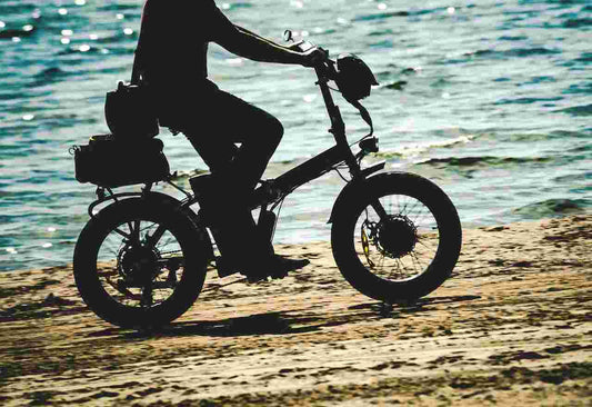 Silhouette of a person riding an electric bike on a sandy beach near the water