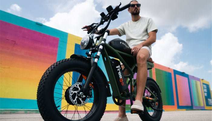 Man riding a black Freego F3 Pro electric bike with fat tires against a colorful wall background
