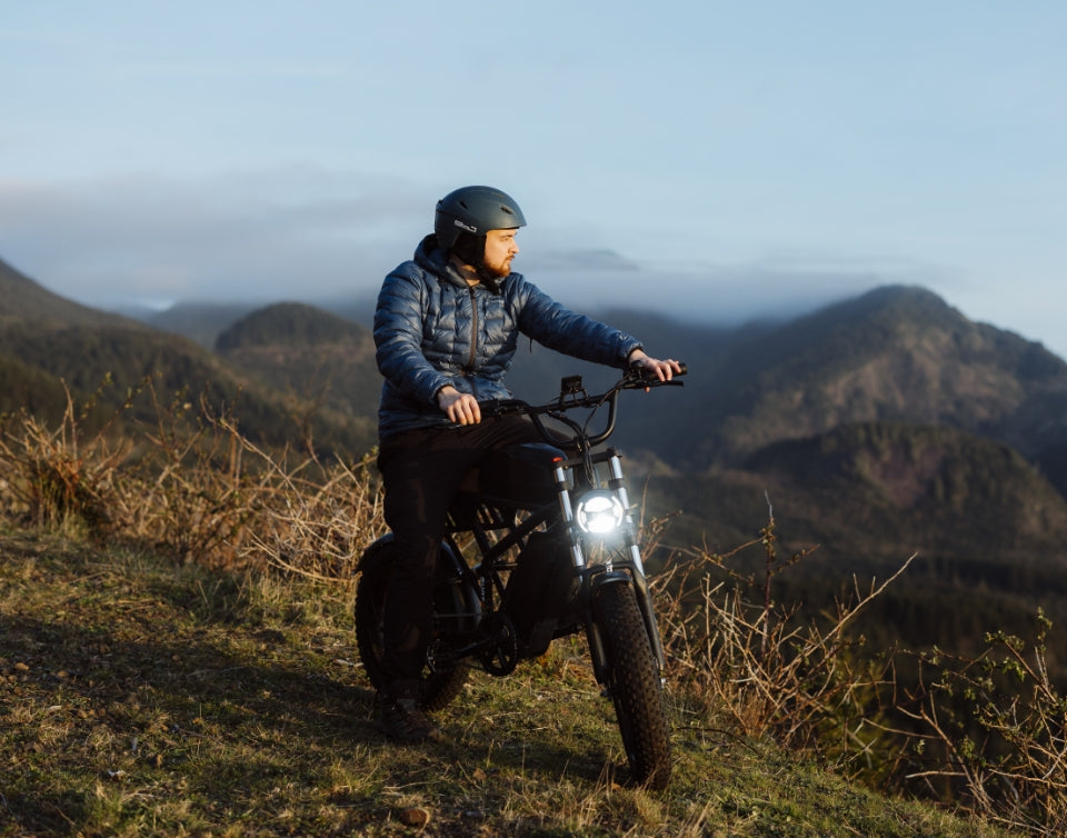 Man riding a Freego e-bike on a mountain trail at sunset, wearing helmet and jacket.