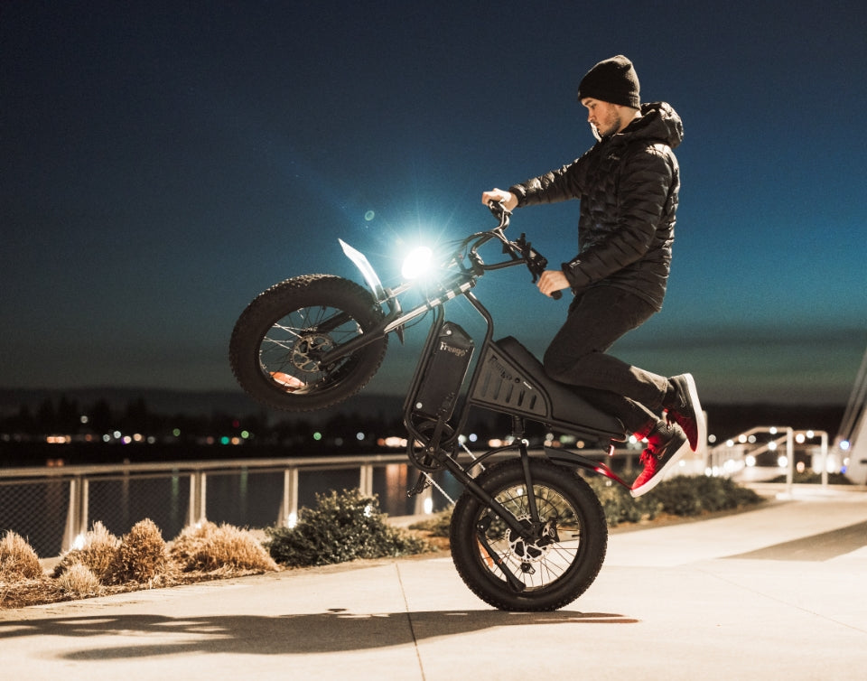 Man performing a wheelie on a Freego e-bike at night near a waterfront.