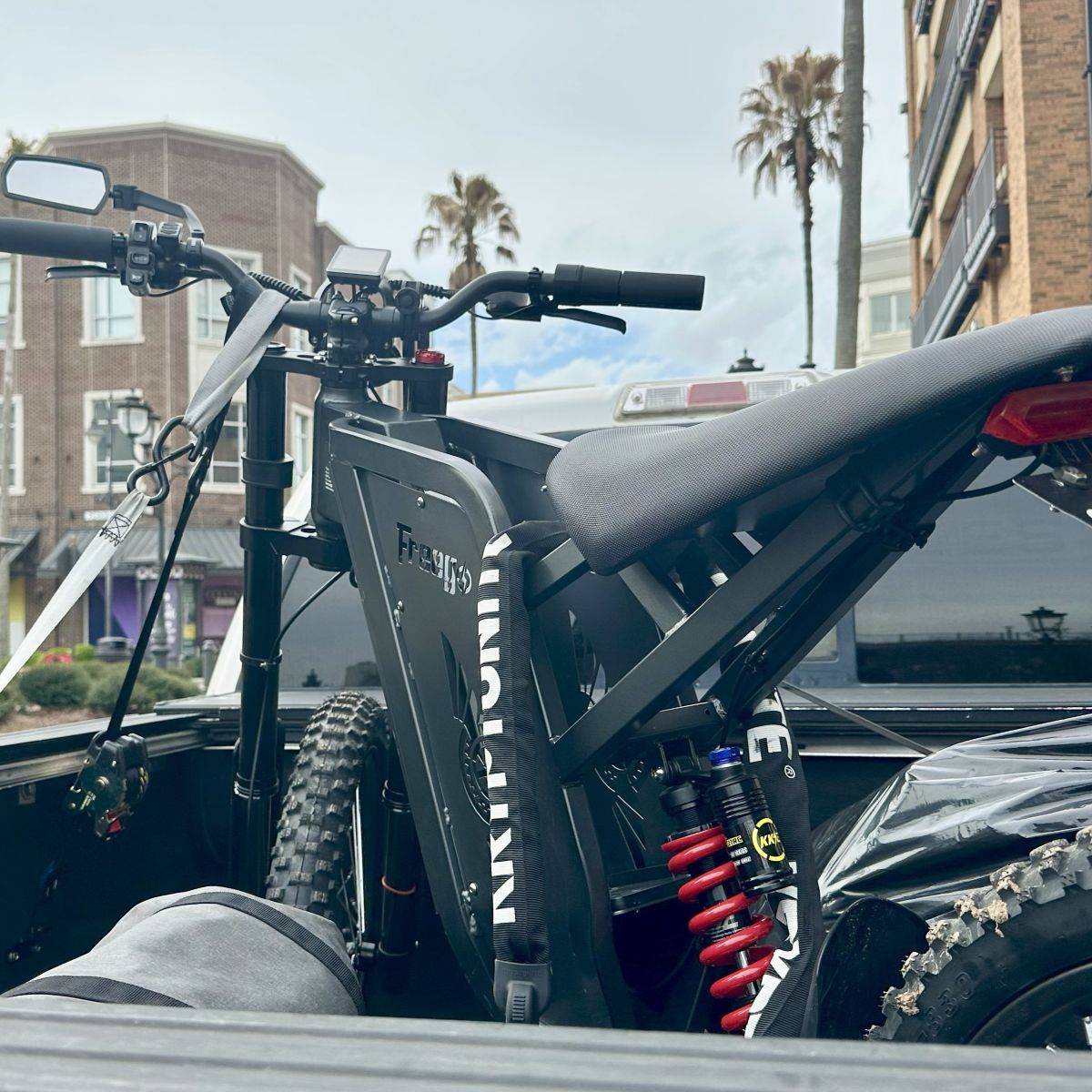 Electric bike on a truck bed with buildings and palm trees in the background