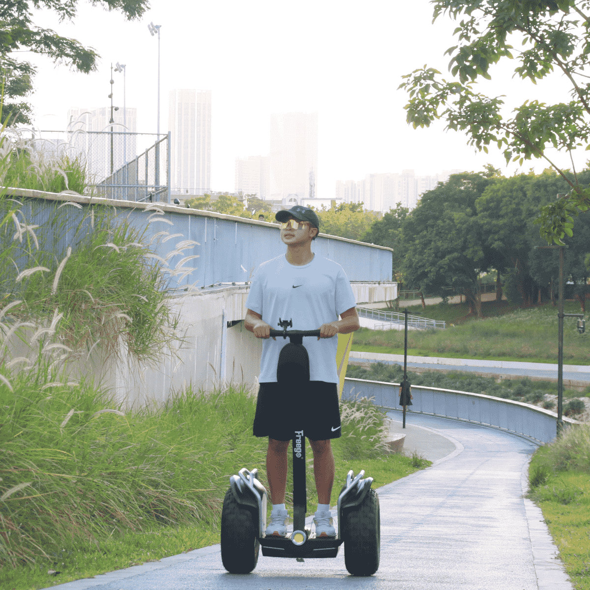 Person riding a Segway in an outdoor setting with greenery and a building in the background
