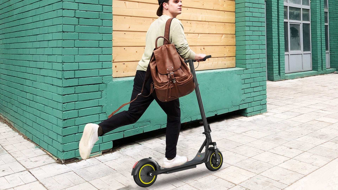 Young man riding an electric scooter wearing casual clothes and a backpack near green and wooden buildings, illustrating safety tips for riding an electric scooter.