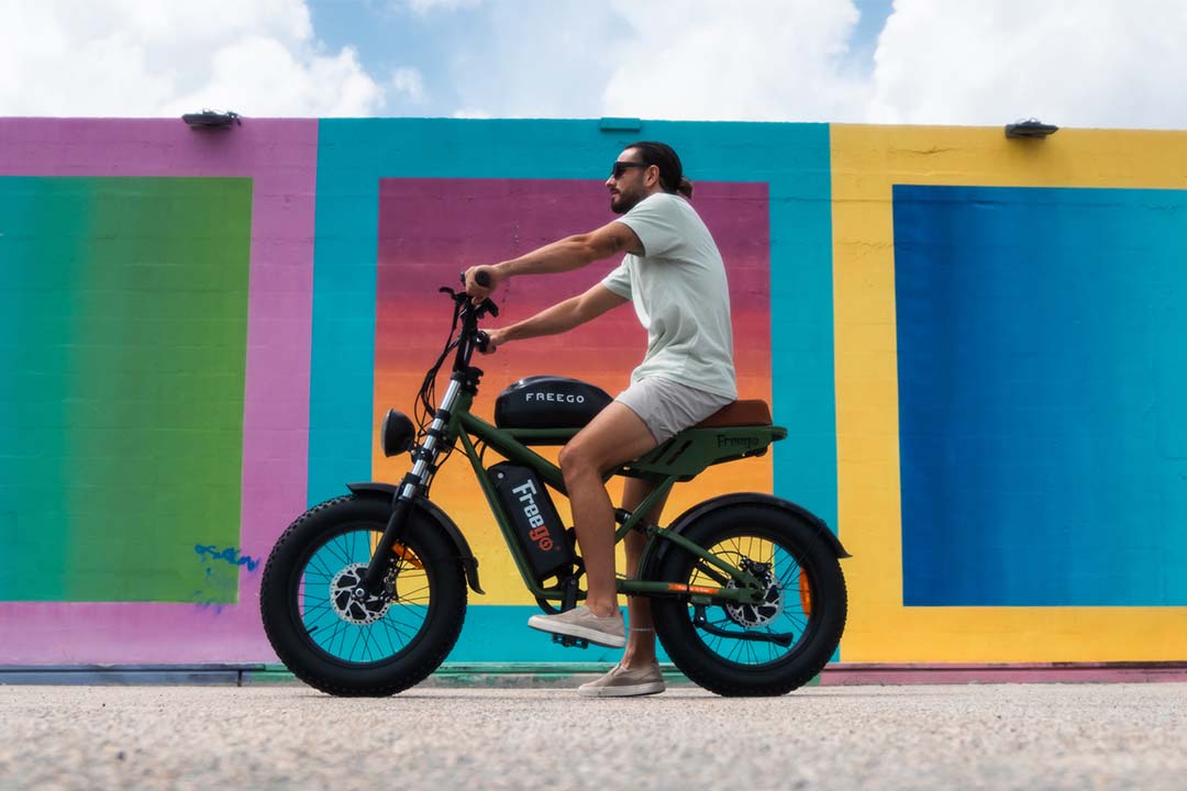 A man sitting on a black Freego F3 Pro against the colorful wall, ready to turn heads of the whole school!