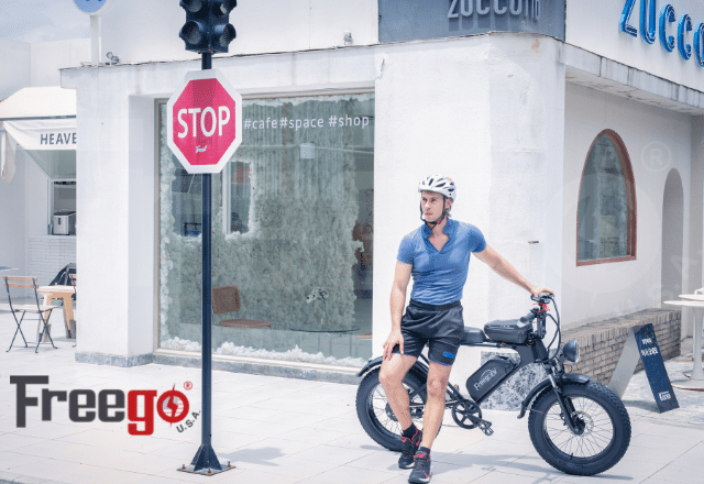 Man wearing helmet sitting on black FreeGo DK200 electric bike near stop sign outside a cafe