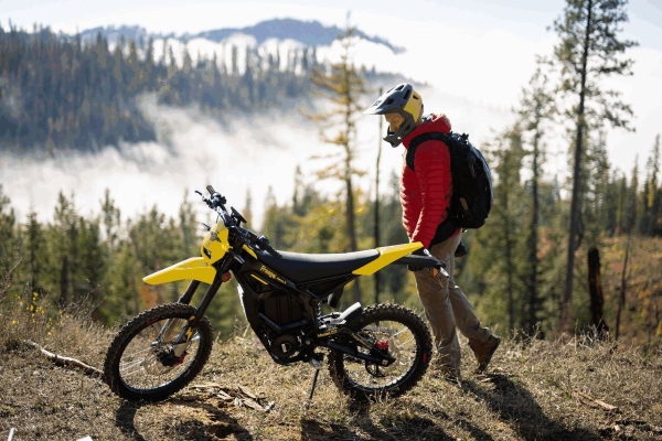 Person with a Freego Nova 5 dirt bike in a forested area with mountains in the background