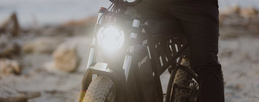 Electric bike with front light on and rider standing beside it on a dirt path, illustrating e-bike motor issue troubleshooting.
