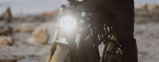 Electric bike with front light on and rider standing beside it on a dirt path, illustrating e-bike motor issue troubleshooting.