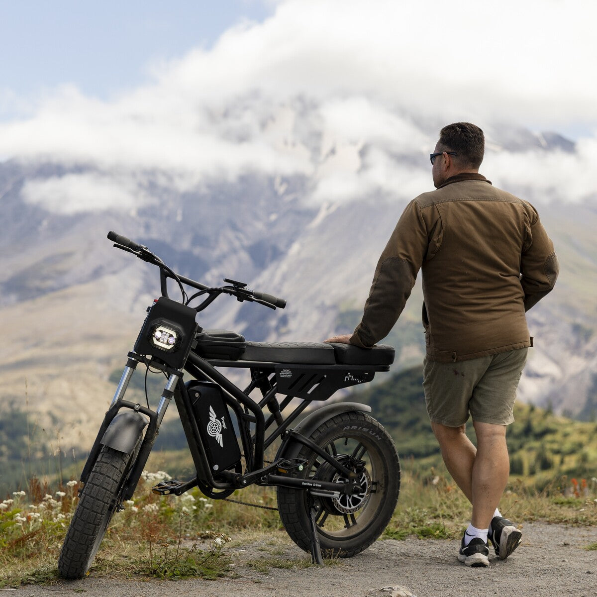 Man standing next to a black electric bike with mountains in the background