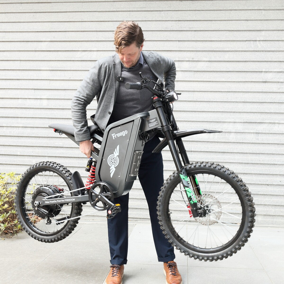 Person holding a black electric bike with 'Frogg' branding against a gray wall.