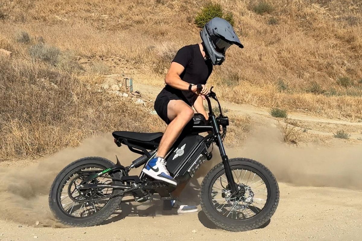 Person riding a black electric bike on a dirt road with a helmet on.