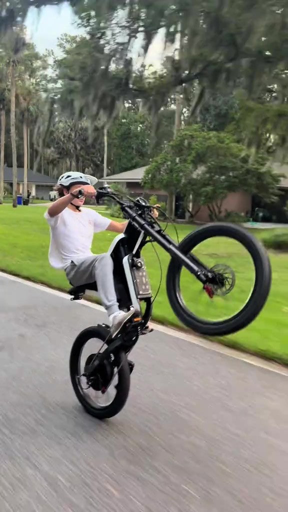 Person riding a black Freego X2 electric bike on a paved path with greenery in the background