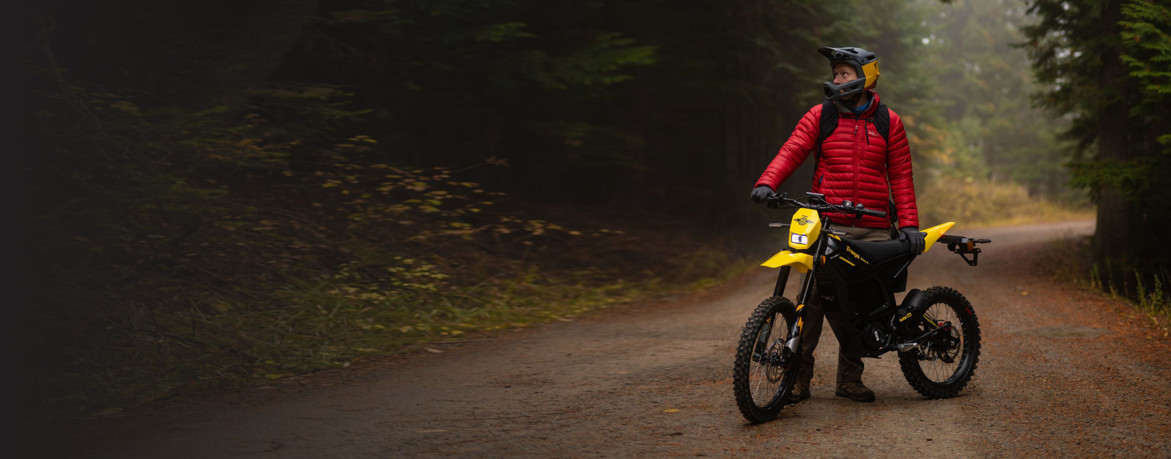 A man in  red jacket and a helmet poses with a Nova 5 on a forest road.
