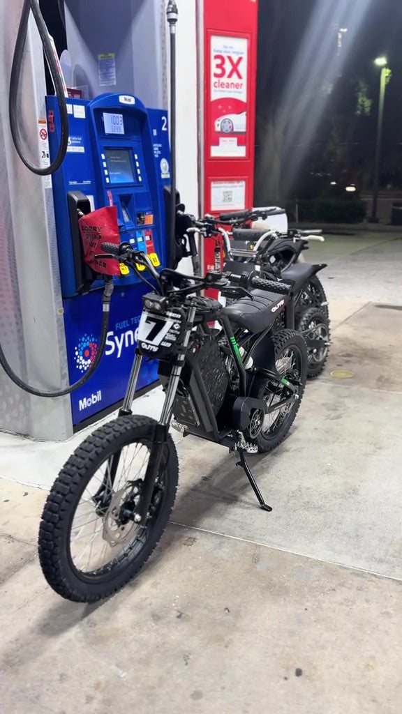Electric bike parked next to a gas pump at a gas station.
