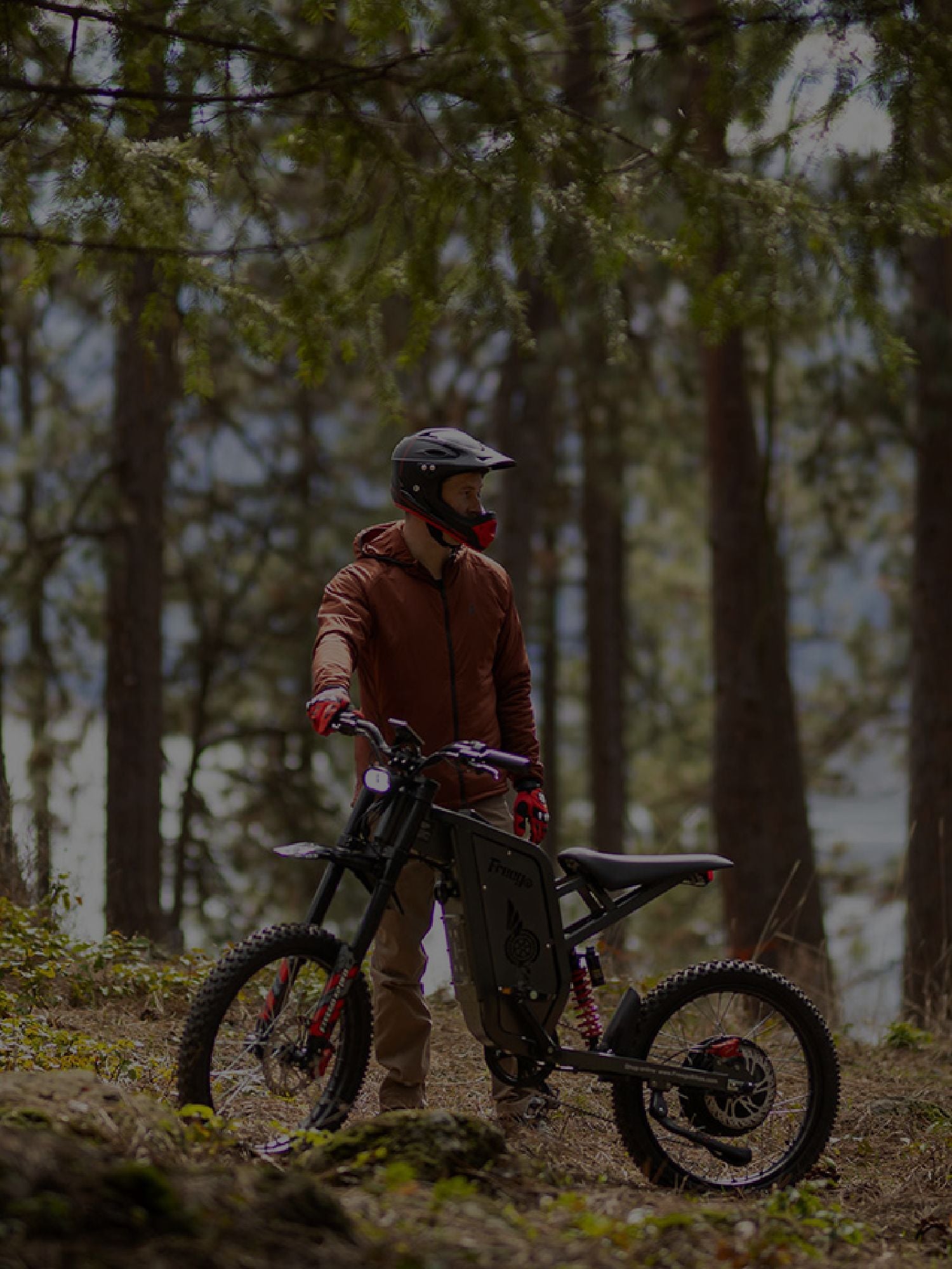A person in orange clothing and a helmet is posing with an X2 Pro in mountainous terrain with many trees in the background.
