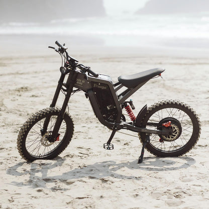 Freego electric dirt bike parked on a sandy beach, showcasing rugged off-road design against a scenic coastal backdrop.