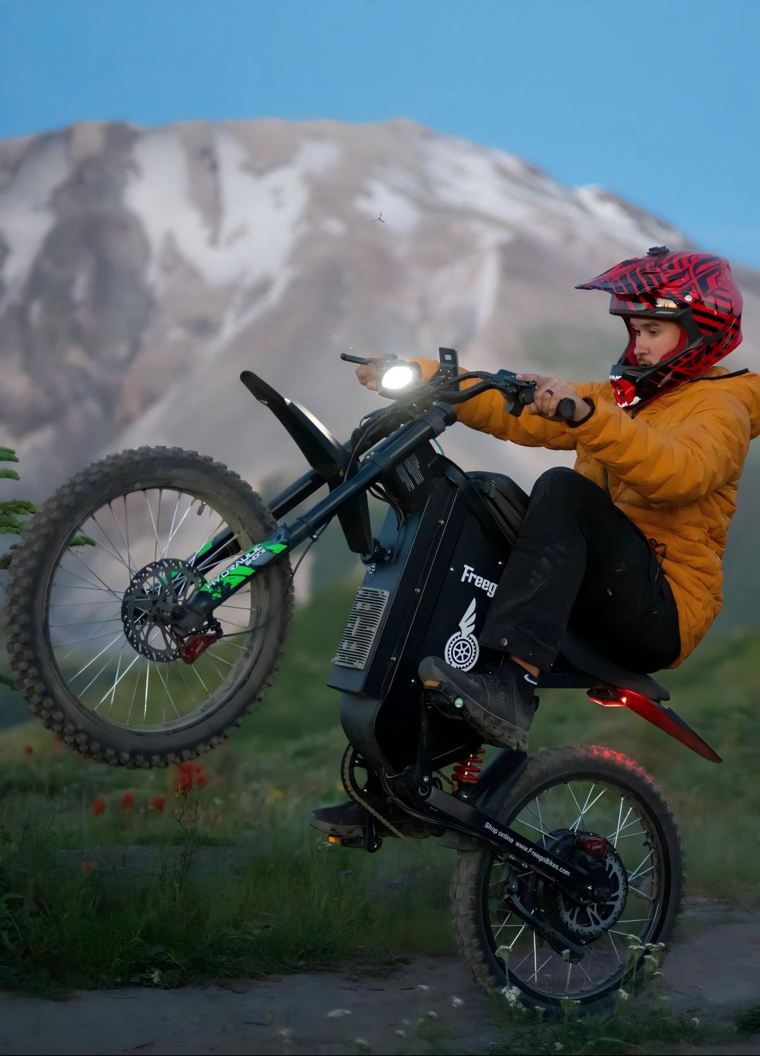 A rider performing a wheelie on a Freego adventure e-bike in a mountain landscape, showcasing its powerful motor, off-road capability, and adventure-ready design.