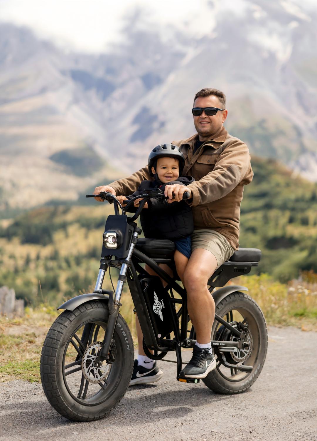 A father and a kid riding together on a Freego fat tire electric bike on a mountain road, showcasing a comfortable family-friendly eBike design for outdoor adventures.