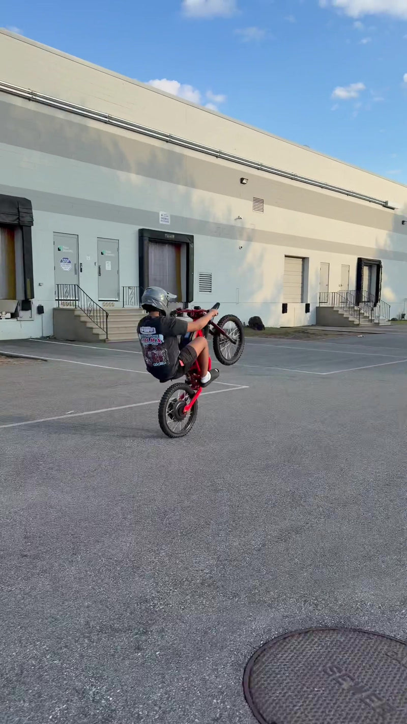 Vertical outdoor action shot of TikTok influencer lamontson performing wheelie stunt on red Freego electric bike in warehouse parking lot