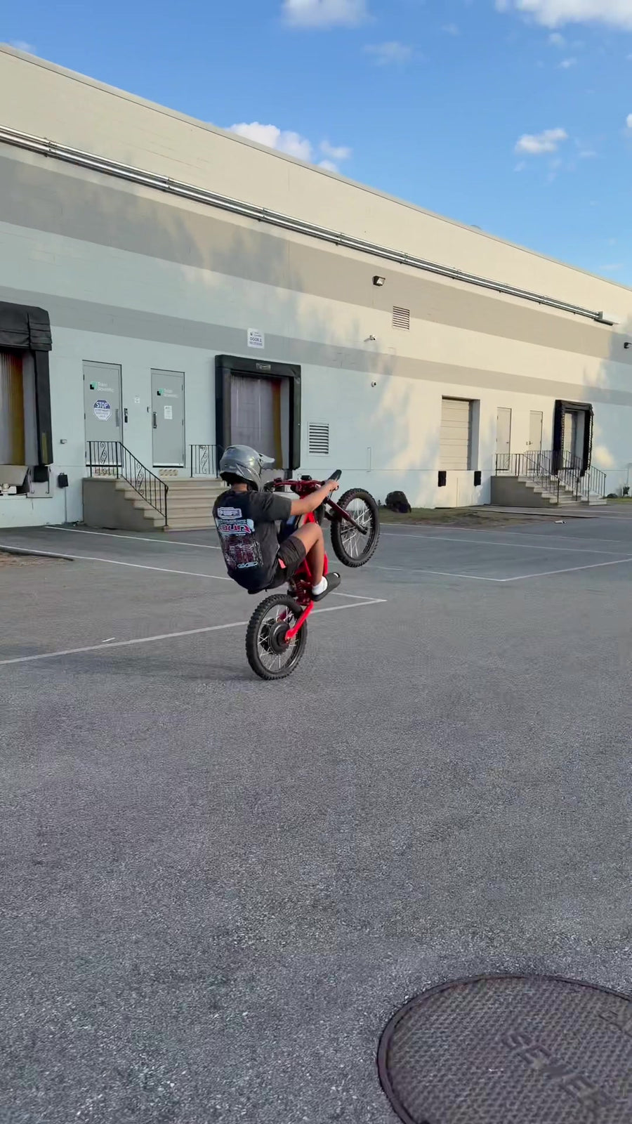 Vertical outdoor action shot of TikTok influencer lamontson performing wheelie stunt on red Freego electric bike in warehouse parking lot