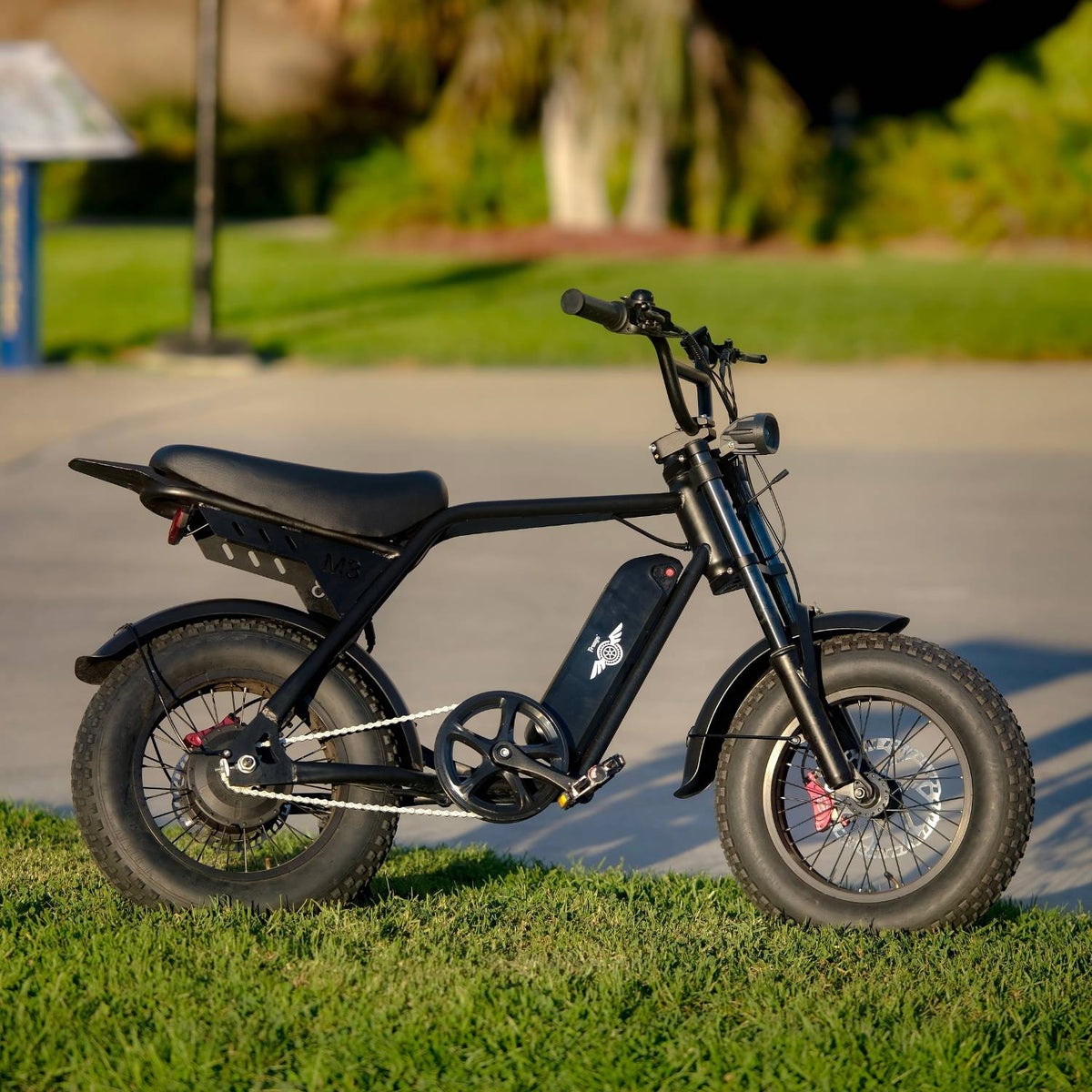 Black Freego M3 electric mini bike parked on grass with trees in the background.