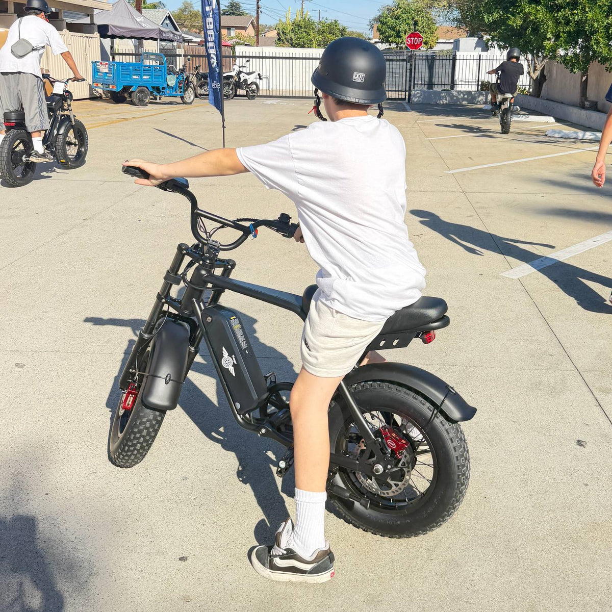 Rear view of a helmeted rider seated on a Freego M3 electric mini bike in a sunny parking lot.