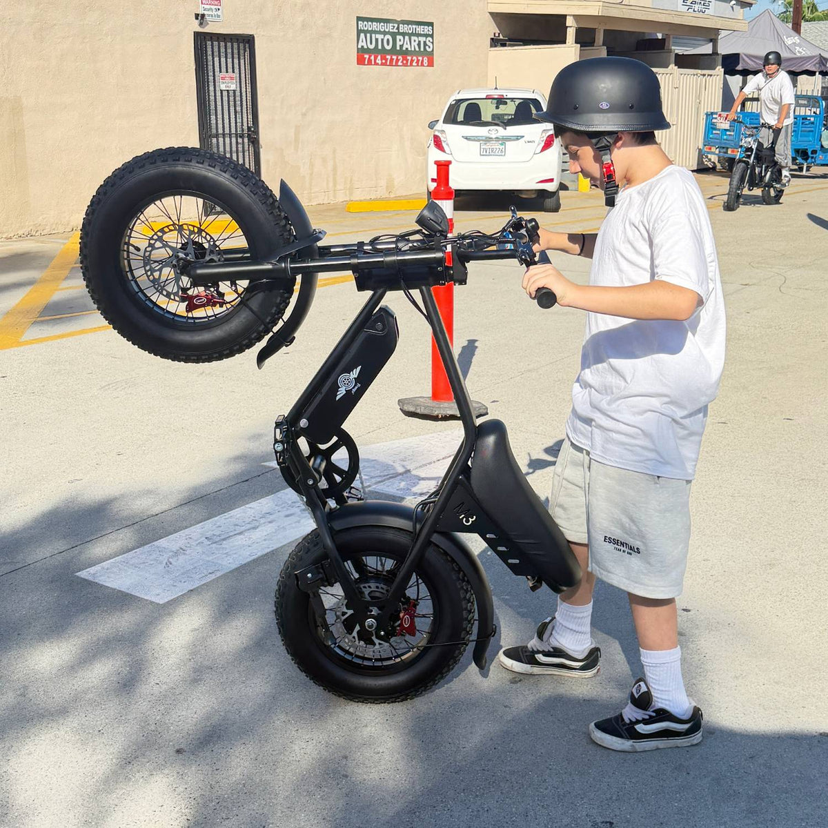 Helmeted rider standing beside a Freego M3 electric mini bike raised vertically on its rear wheel.