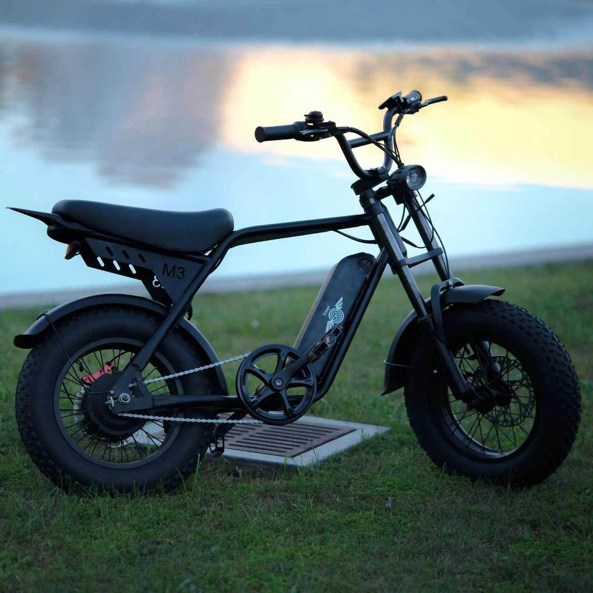 Black Freego M3 electric mini bike parked on grass beside the water at sunset.