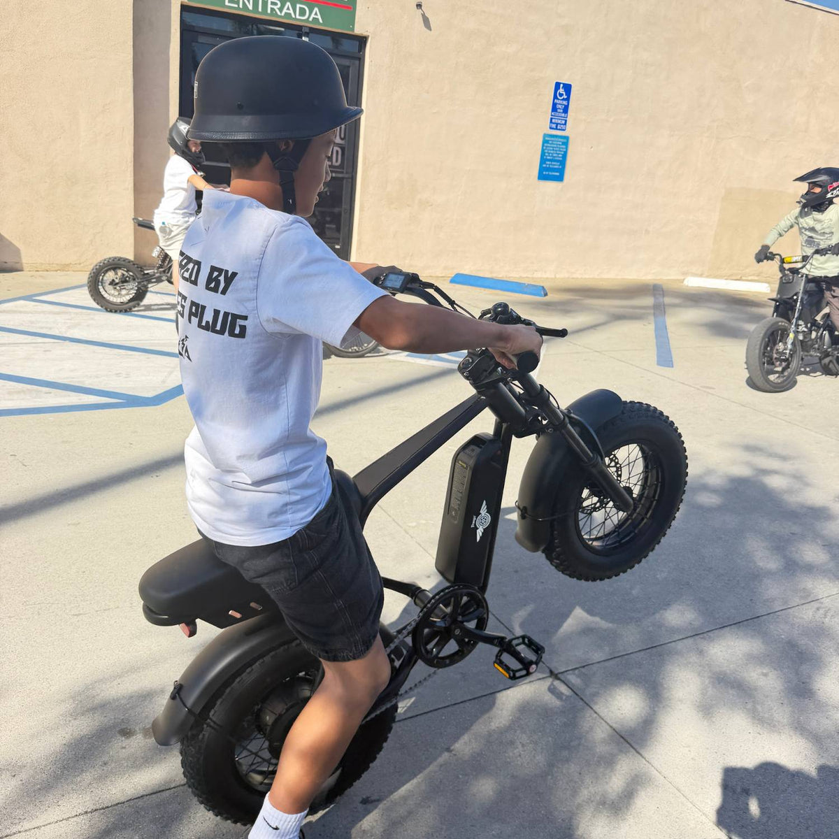 Helmeted rider performing a wheelie on a Freego M3 electric mini bike in a parking lot.
