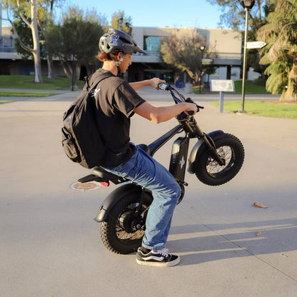 Side view of a helmeted rider performing a wheelie on a Freego M3 electric mini bike.
