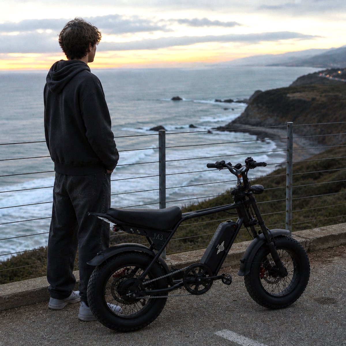 Young rider standing beside a Freego M3 fat tire e-bike at a coastal overlook