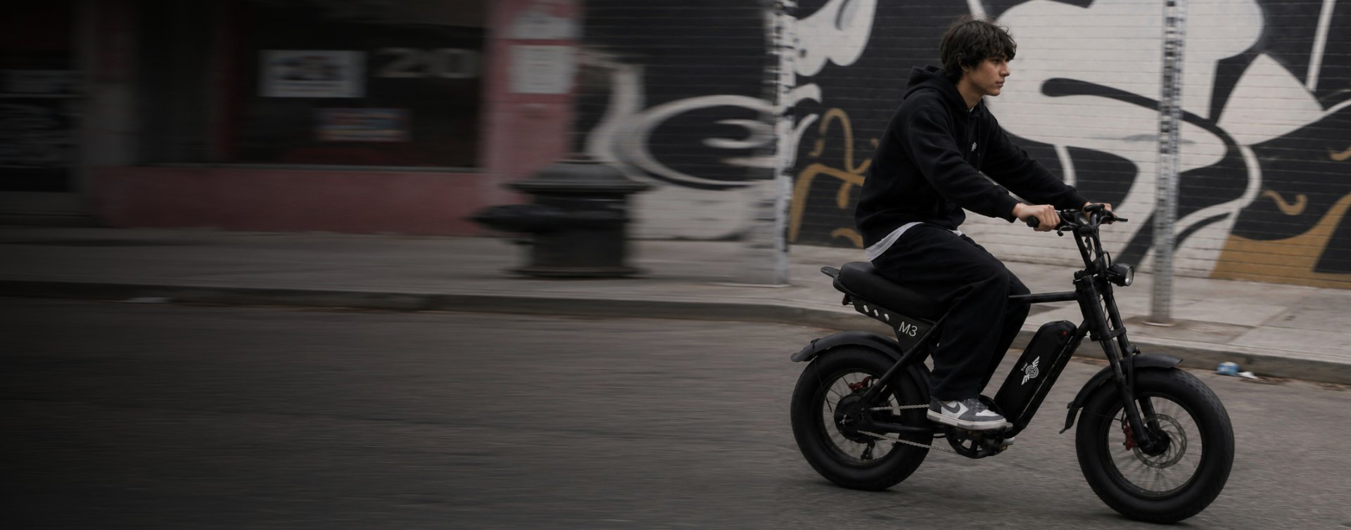 Young rider commuting on a Freego M3 fat tire e-bike along a graffiti-lined city street