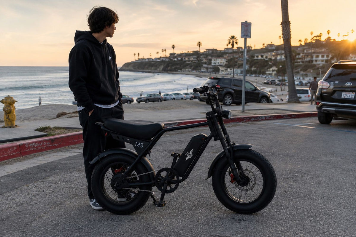 Young rider standing beside a Freego M3 fat tire e-bike near the beach at sunset