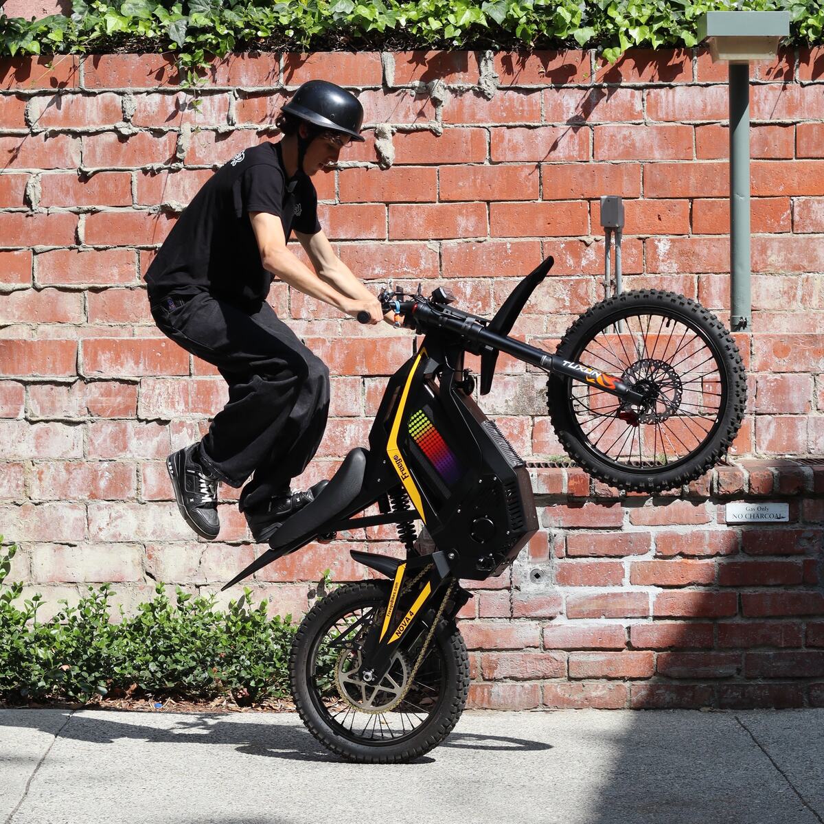 Freego Nova 4 electric bike rider performing a wheelie jump onto the seat against a brick wall
