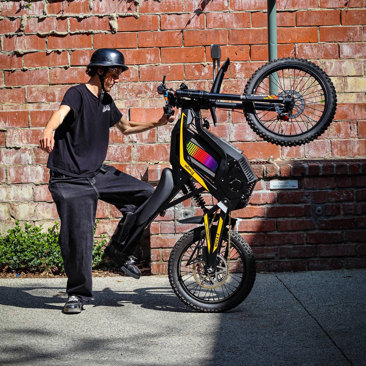 Freego Nova 4 electric bike wheelie step-off action shot in an urban setting against a brick wall