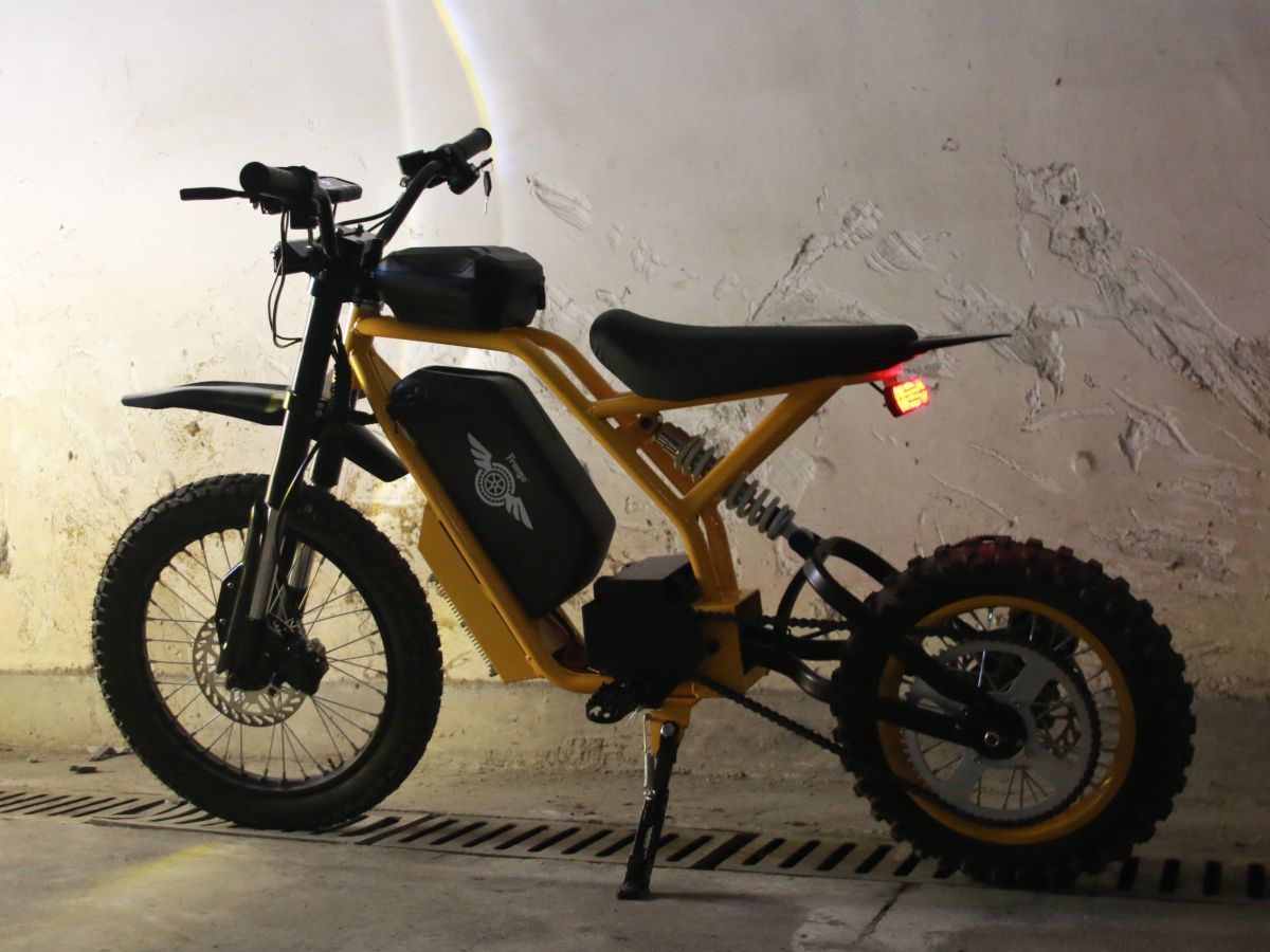 Yellow electric bike with black seat against a textured wall.