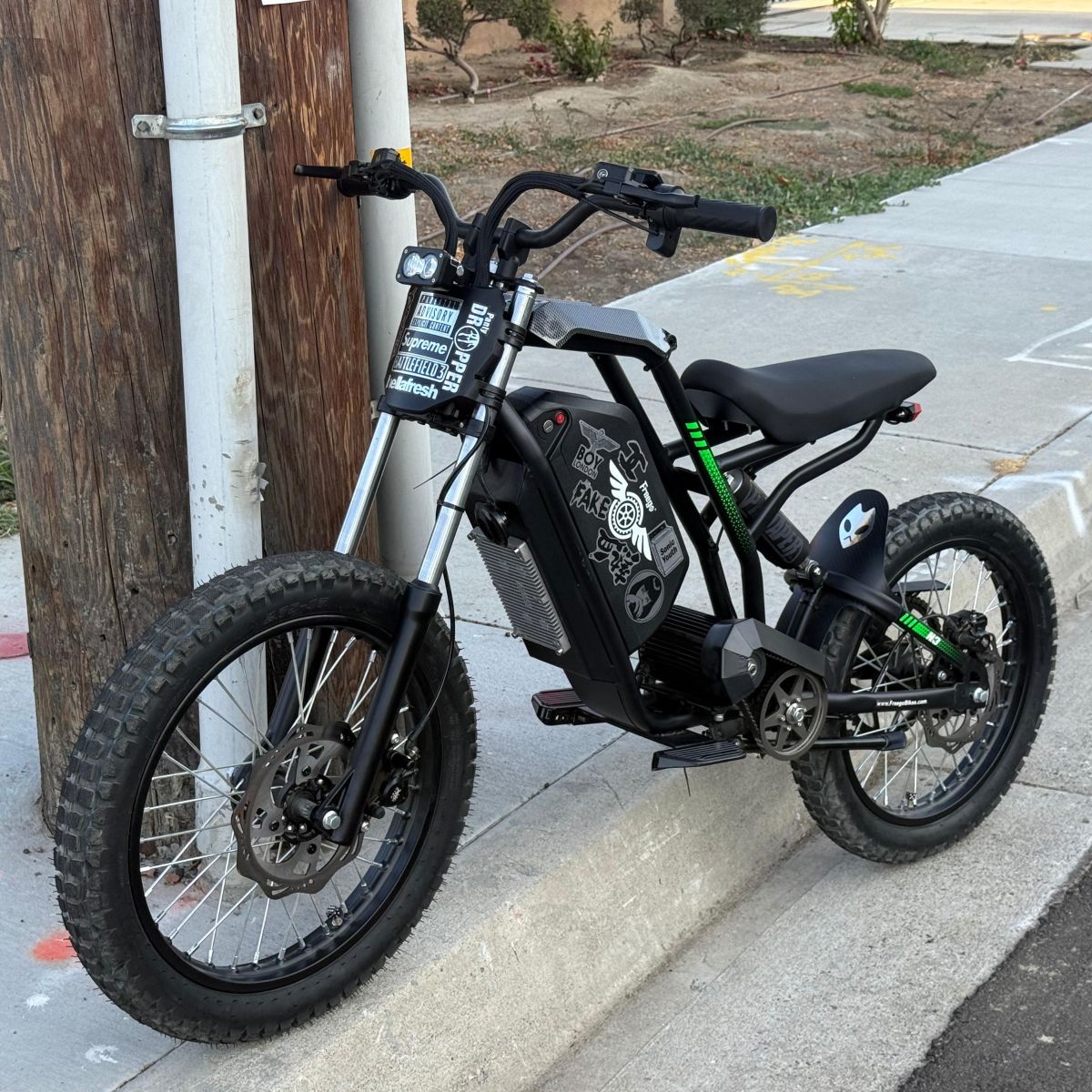Black electric bike parked on a sidewalk next to a wooden post.