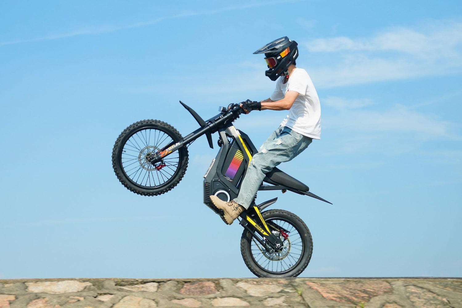 Rider performing wheelie on Freego Nova4 electric dirt bike against clear blue sky