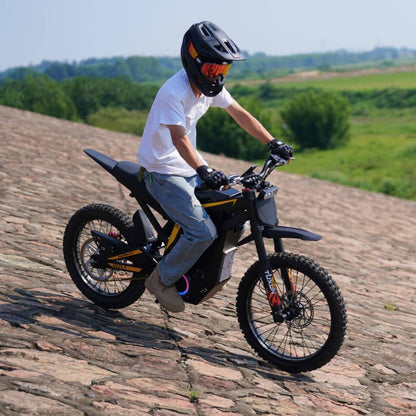 Rider riding Freego Nova4 electric dirt bike on stone slope with green field background