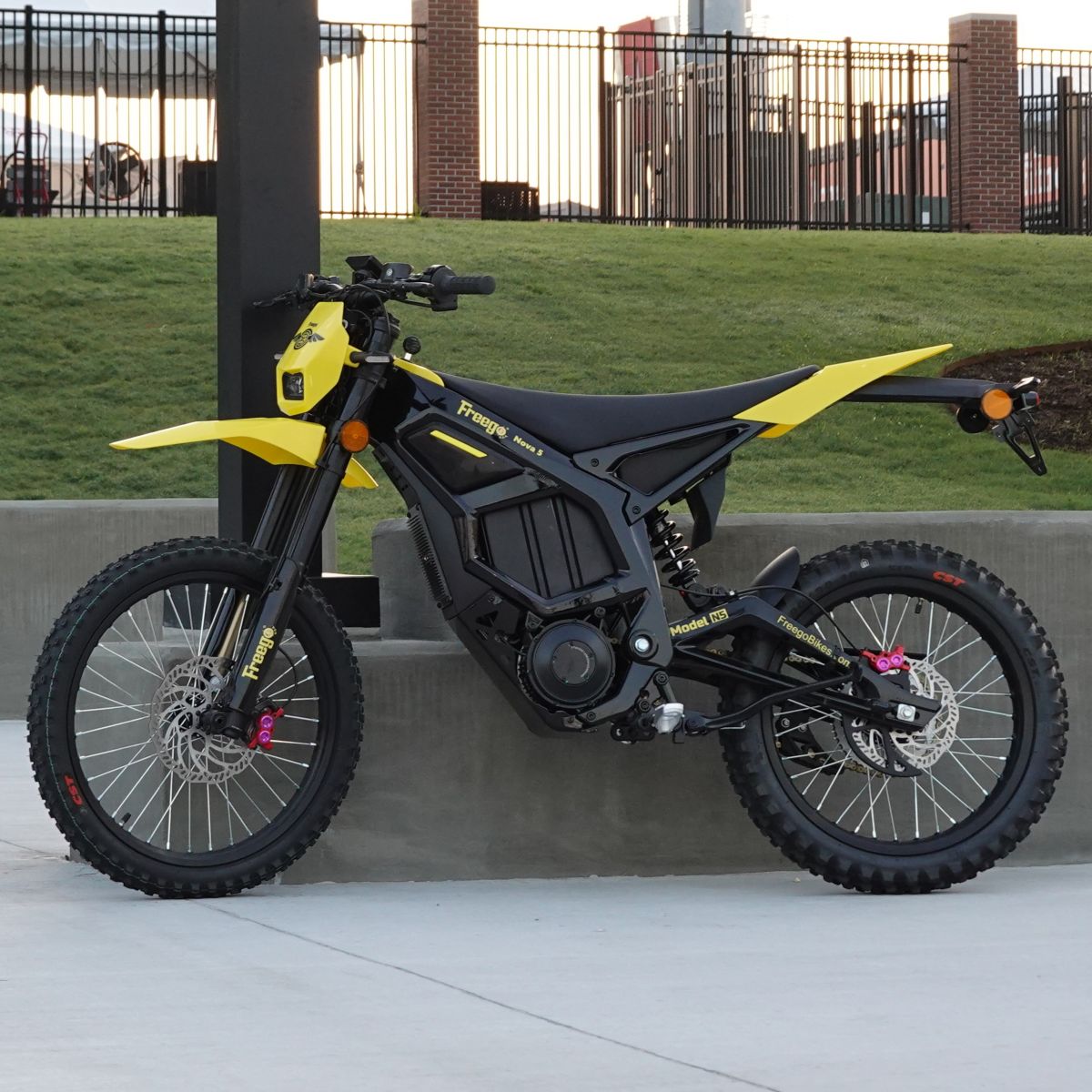 Yellow and black electric bike on a concrete surface with grass and a fence in the background