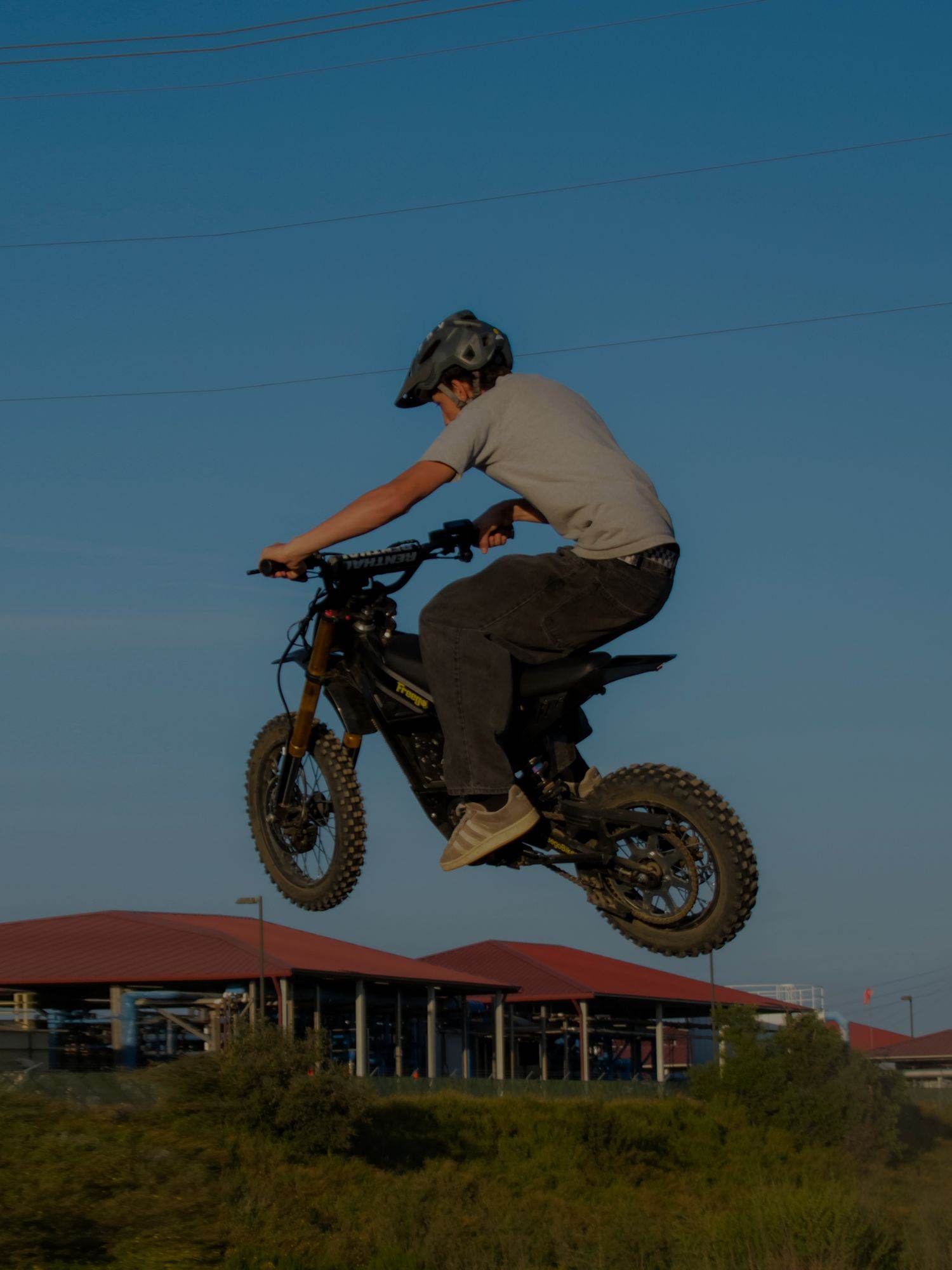 Person riding a Nova 5 Mini dirt bike in the air against a clear blue sky.
