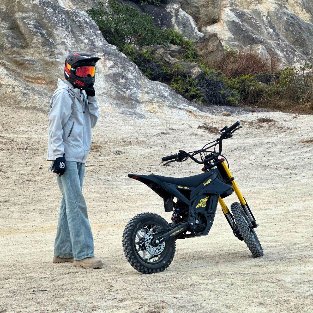 Person with a helmet standing next to a Nova 5 Mini ebike in a rocky outdoor setting