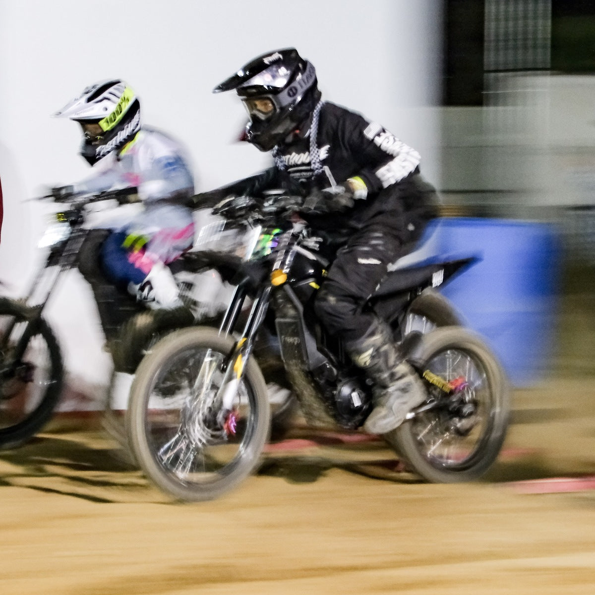 Motion blur action photo of two racers competing on dirt track at night, primary rider riding Freego Nova5 electric dirt bike