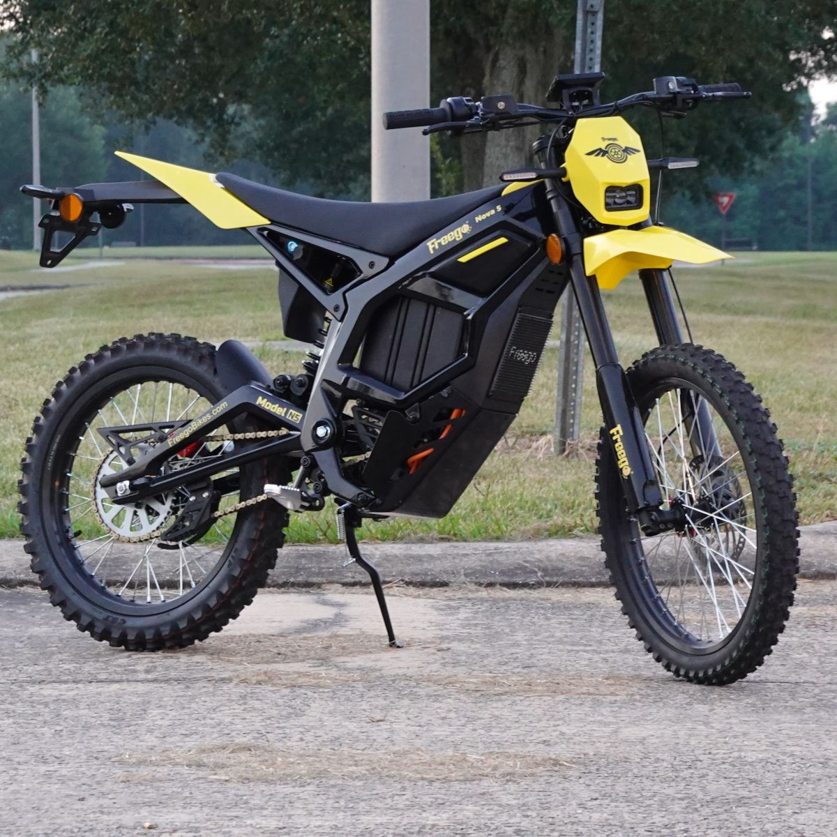 Black and yellow electric bike on a paved road with grass and trees in the background