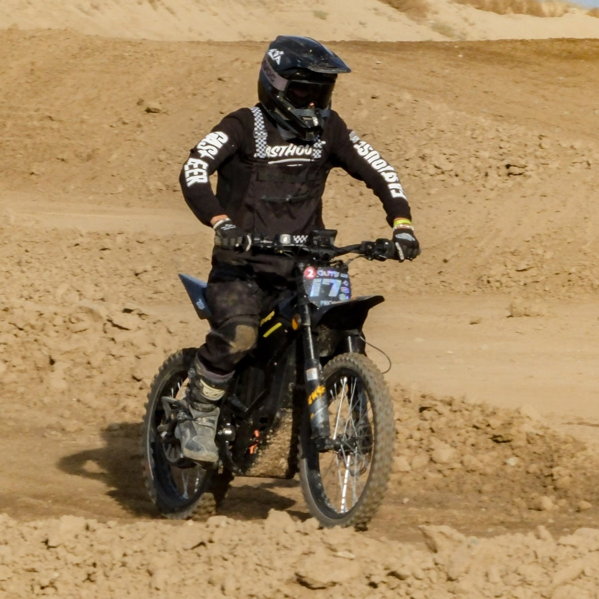 Side view of rider in full motocross gear riding Freego Nova5 electric dirt bike on rough sandy motocross track, dry dirt hills background.