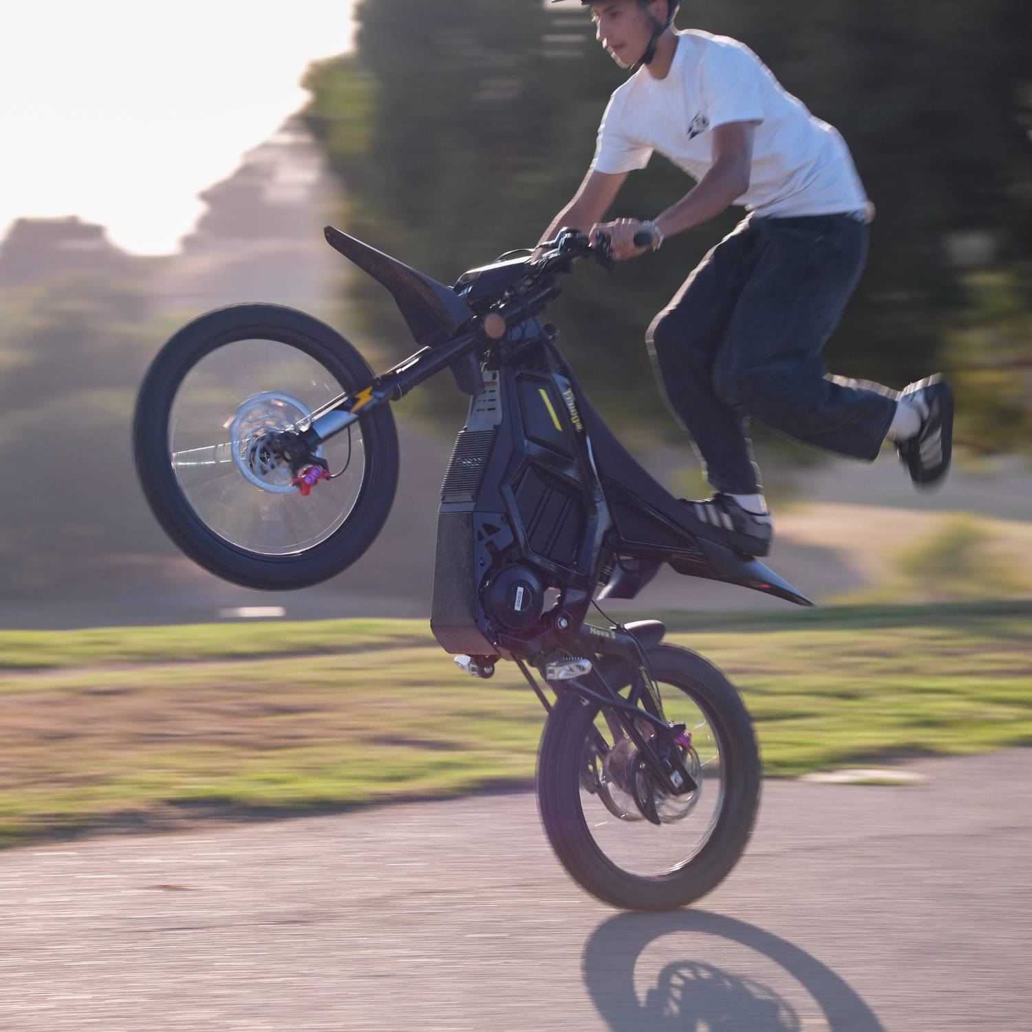 Rider performing one-legged wheelie stunt on Freego Nova5 electric dirt bike with motion-blurred outdoor background