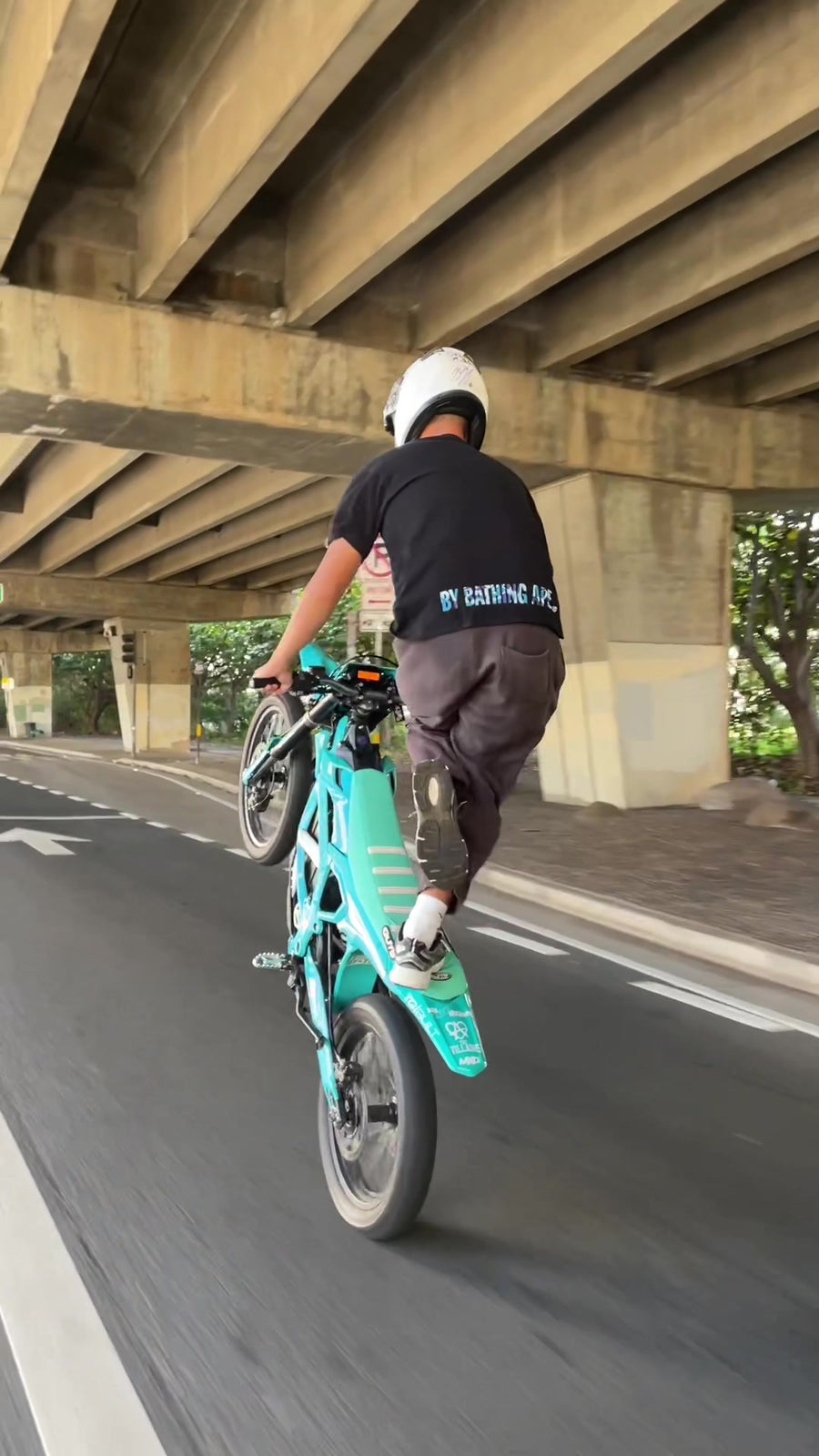 Rear view action shot of rider doing wheelie on turquoise Freego Nova5 electric dirt bike under highway overpass on city road