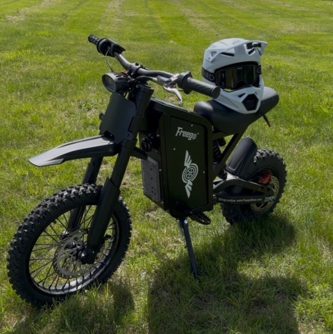 Freego X0 electric dirt bike parked on green grass with helmet on seat