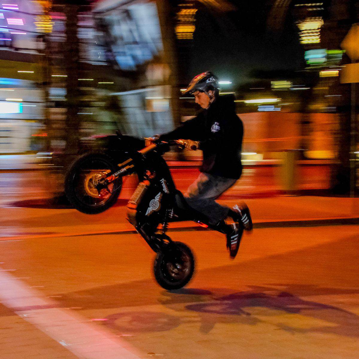Person riding a Freego X0 Mini ebike on a city street at night with blurred lights in the background